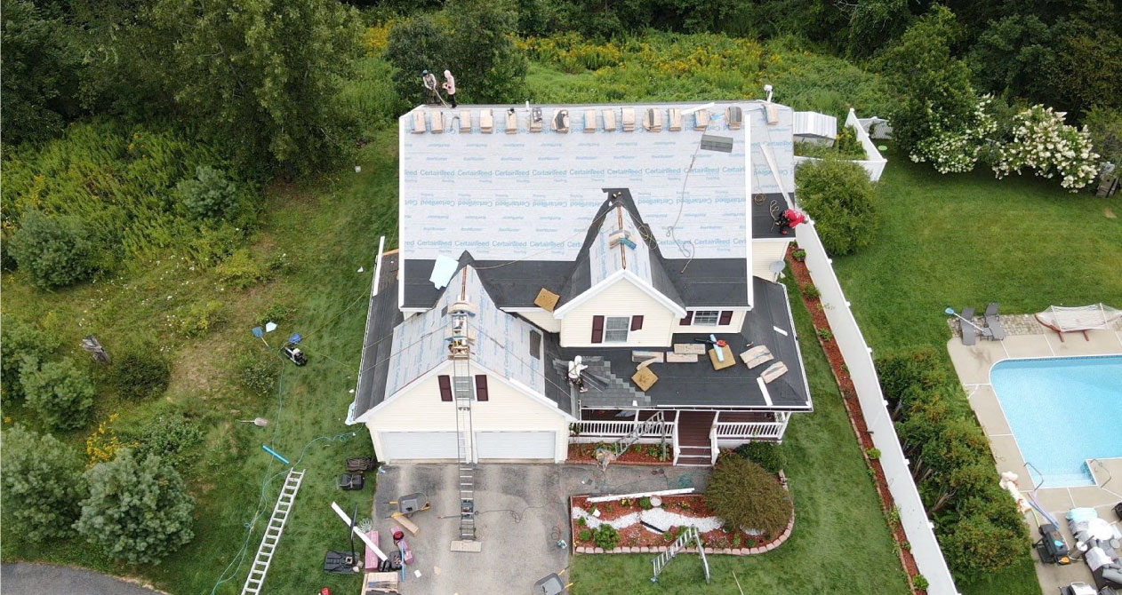 A house undergoing roof replacement with workers installing new shingles, provided roofing services in Boston by CAN Roof