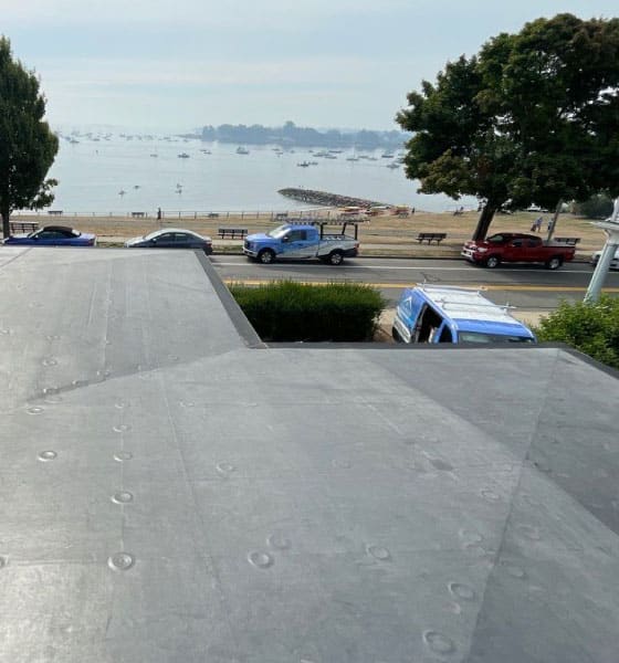 A newly installed rubber roofing system on a flat roof, overlooking a scenic waterfront with service vehicles nearby