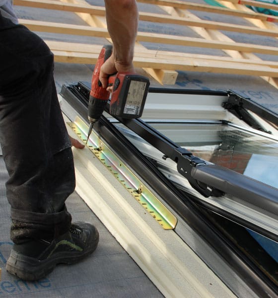 A worker using a power drill to secure a new skylight frame on a roof, ensuring skylight replacement in Boston