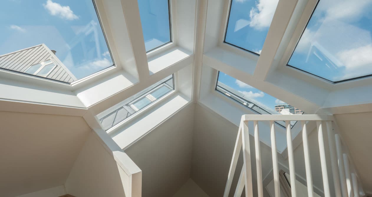 A bright attic space with multiple large skylights, white framing, and a staircase railing, offering skylight services in Boston