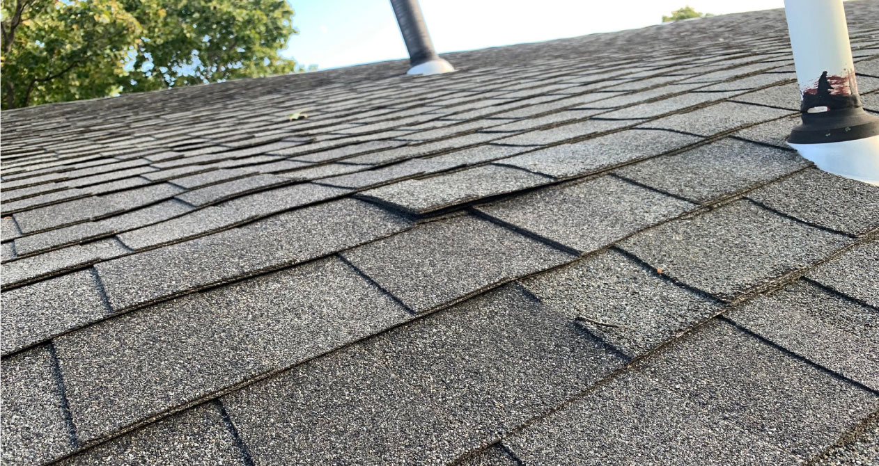 Damaged asphalt shingles with lifted edges and visible wear, indicating the need for a roof inspection in Boston MA