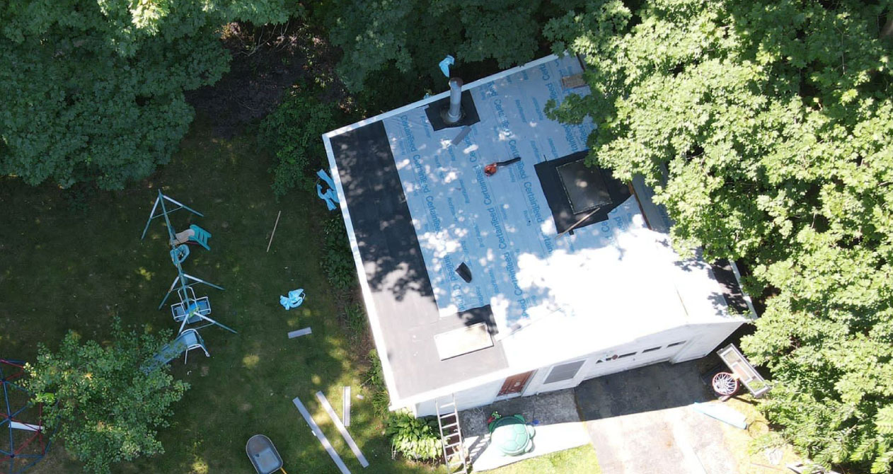 A small building with a partially completed roof covered in underlayment and tools, indicating roof replacement in Boston MA