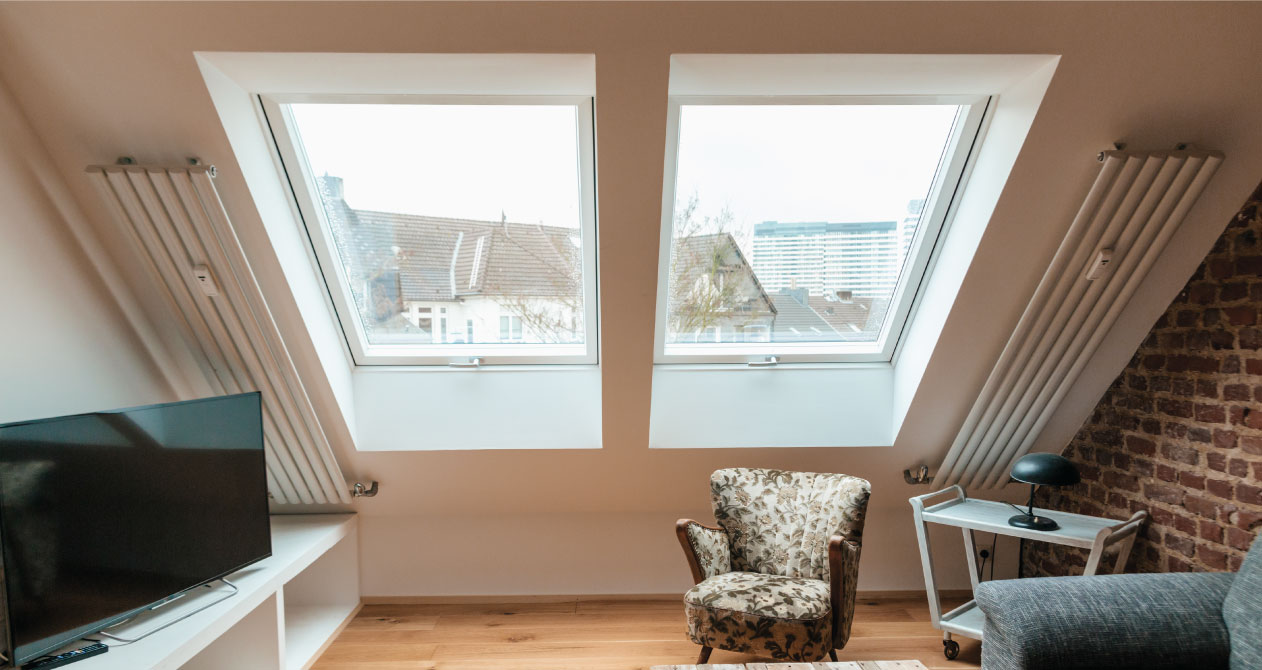 A cozy attic living space with two large skylights bringing in natural light, featuring skylight installation