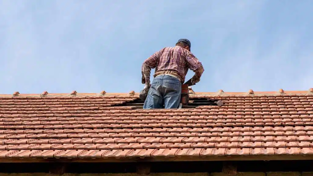 DIY roof repair in progress - man fixing a damaged tile roof with tools, highlighting risks of improper roof maintenance