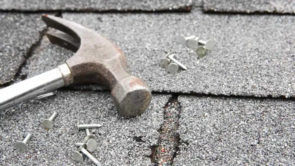 Hammer, roofing nails on grey-colored flat rooftop shingles, asphalt shingles, tools for roof repair