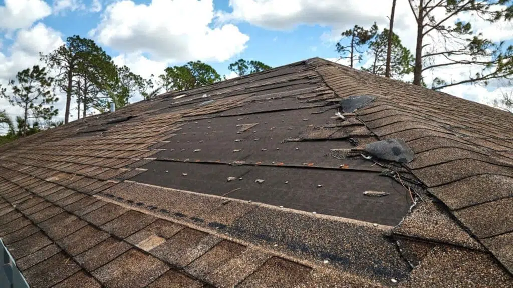 Wind damaged house roof with missing asphalt shingles after hurricane Ian in Florida, repair of home rooftop concept