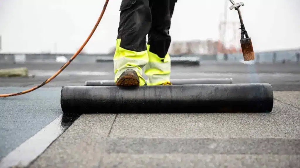 Professional roofer applying tar with blowtorch on new roofing felt for waterproofing a flat roof construction site