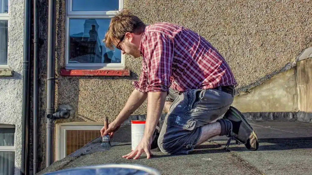 Young male homeowner in red plaid shirt sealing roof of his house, doing DIY, roof maintenance improvement
