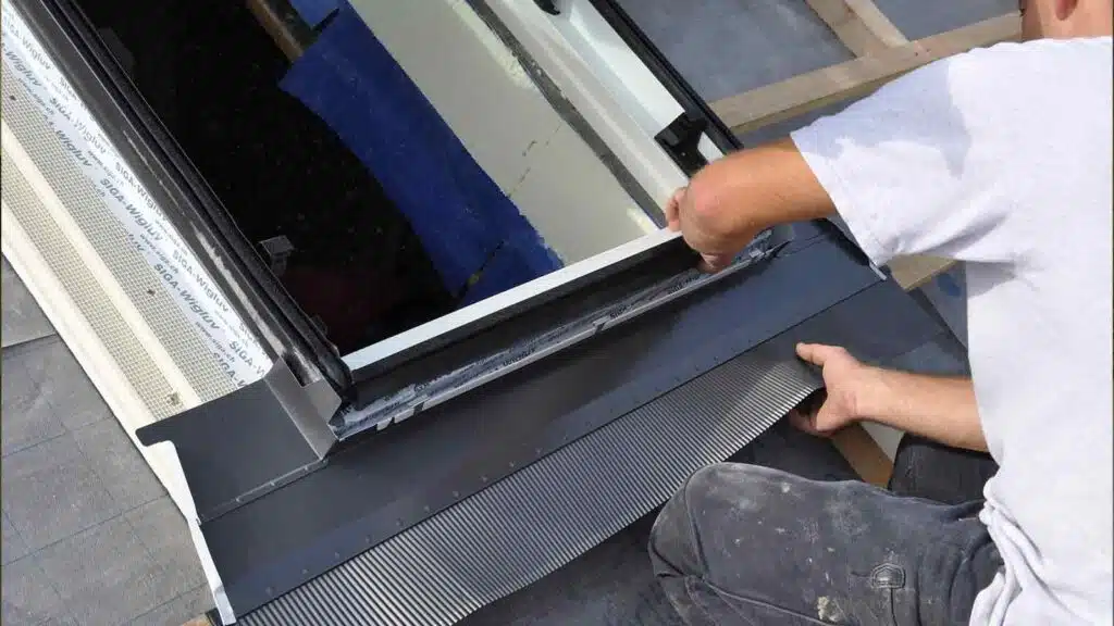 Worker assembling skylight window on roof, sealing edges with flashing to prevent rain leakage