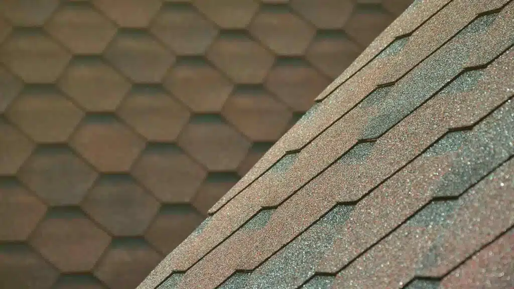 Close-up view of a textured bituminous roof with hexagonal asphalt shingles in brown and green hues.