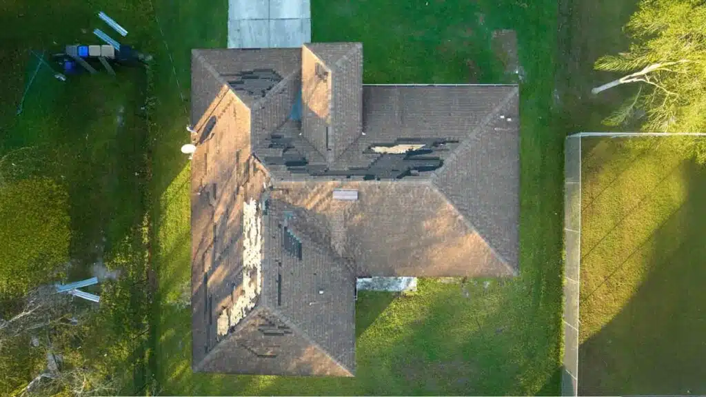 Aerial view of a house roof with severe damage and missing shingles, indicating storm or wind impact.