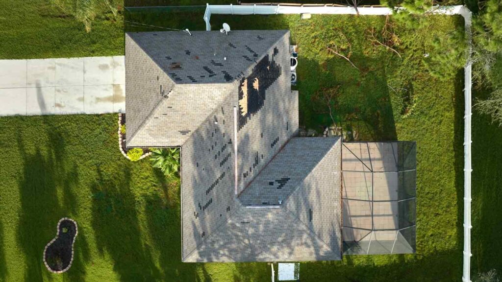 Aerial view of a house with severe roof damage caused by Hurricane Ian, showing missing shingles and debris.