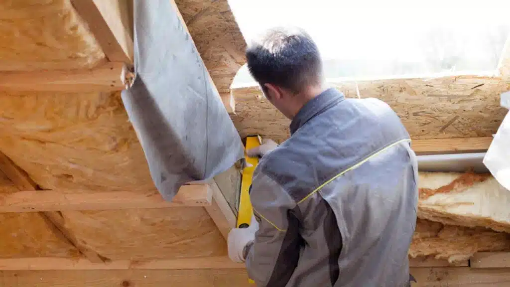 Professional worker installing insulation in a wooden attic, ensuring energy efficiency and proper ventilation.