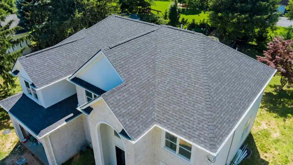 Aerial view of a newly installed asphalt shingle roof on a modern residential house, surrounded by lush greenery.