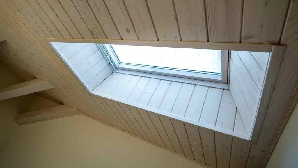 Skylight window set in a sloped wooden ceiling with natural light brightening the attic interior.