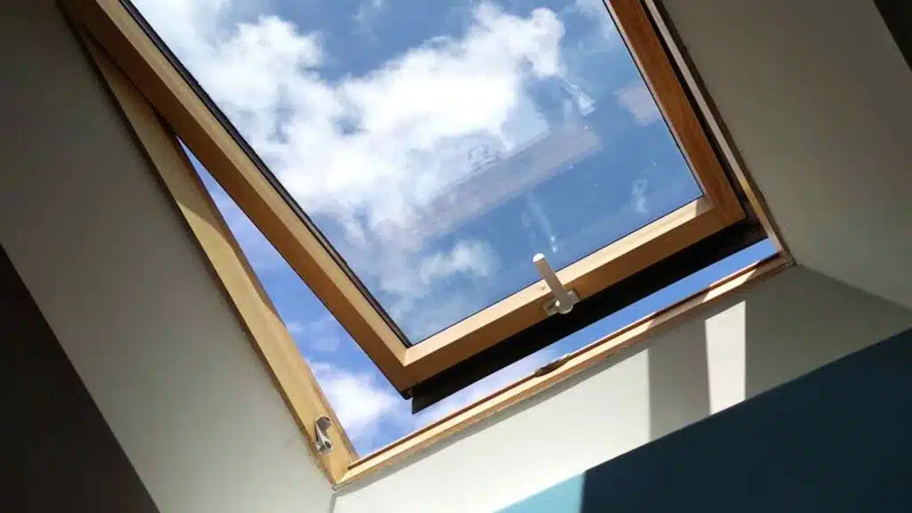Open skylight window with a wooden frame, showing a bright blue sky and clouds, enhancing natural light.