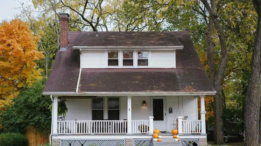 Old white house with a steep roof covered in debris and leaves, indicating the need for a DIY roof inspection.