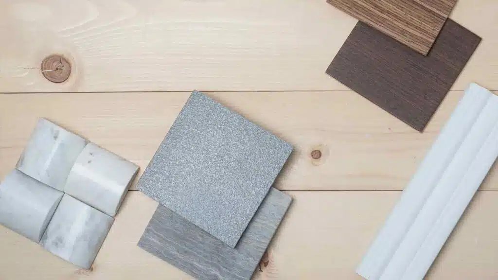 Various material samples including wood, stone, and marble tiles arranged on a light wooden surface.