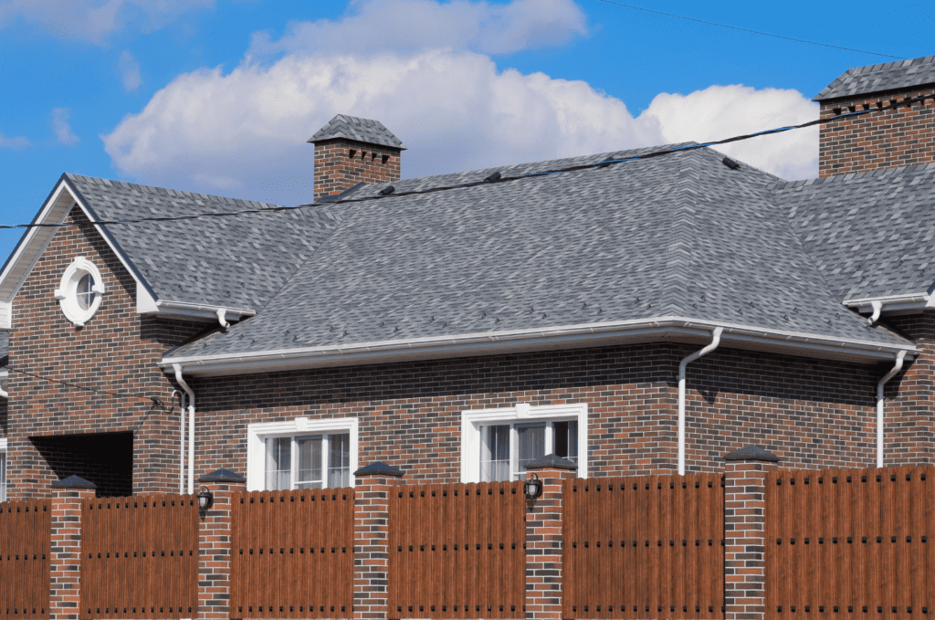 Brick home with a well-maintained asphalt shingle roof, clean ridgelines, and proper drainage under clear blue skies