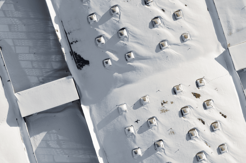 Aerial view of a flat roof with vents under snow, highlighting commercial roof preparation for winter conditions