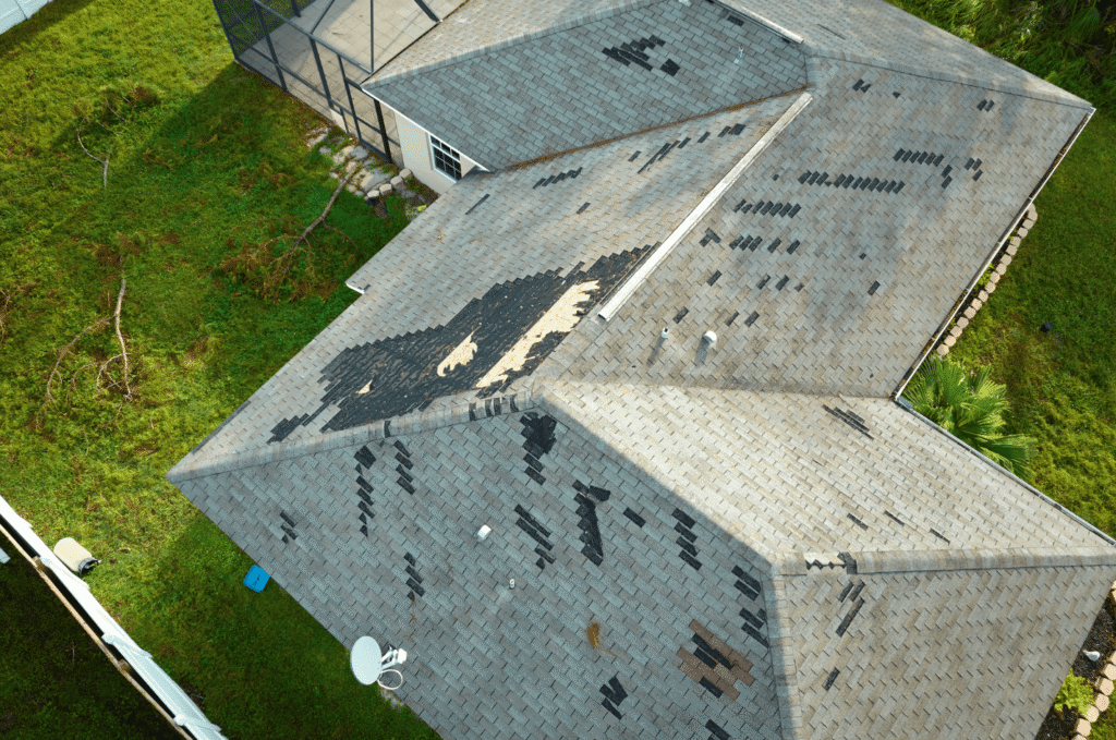 Aerial view of a home showing widespread roof damage, including missing shingles and deteriorated areas across multiple slopes