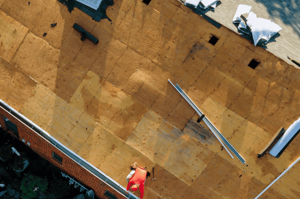 Contractor working on plywood decking during new roof installation while preparing measurements for an accurate roof estimate