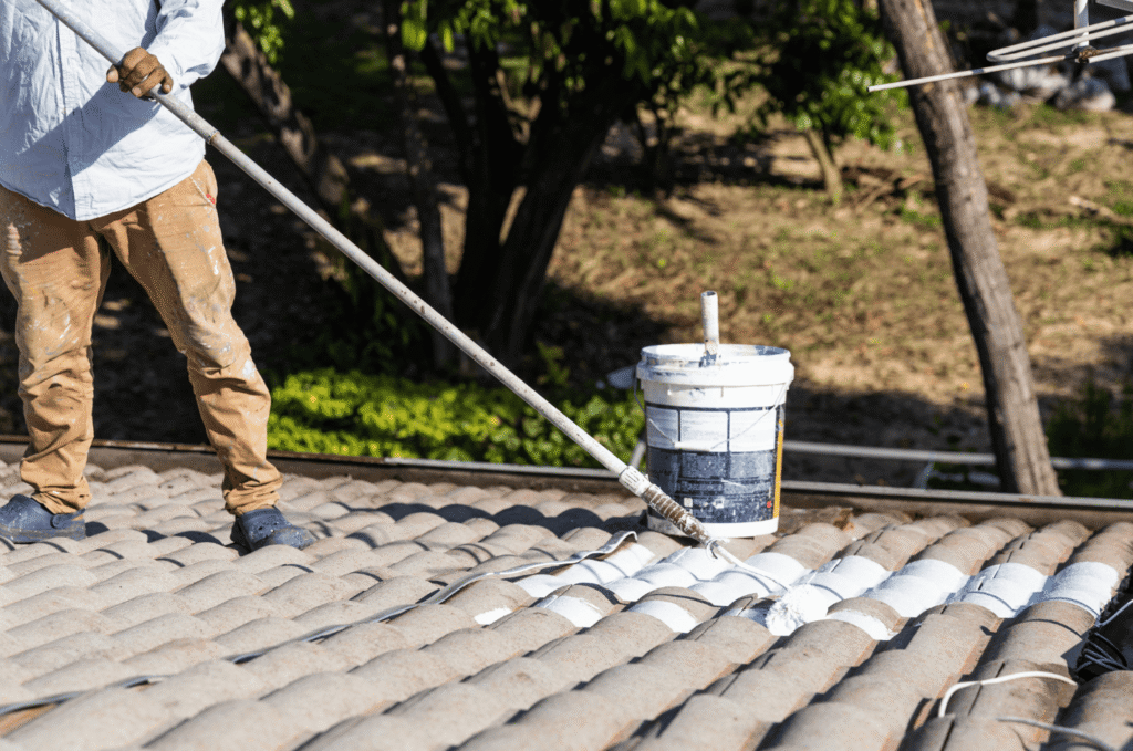 Roofing contractor applying protective roof coating to concrete tiles to seal and extend the roof’s lifespan