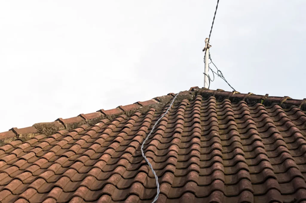 Roof sagging visible along clay tile ridge with uneven lines and structural stress near the peak of the home
