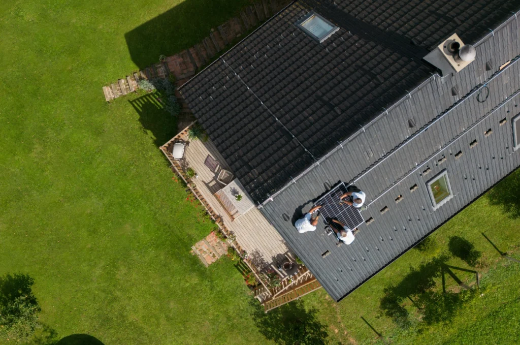 Aerial view of new roof installation with dark shingles and solar panel placement, showing precise layout and secure roofing work
