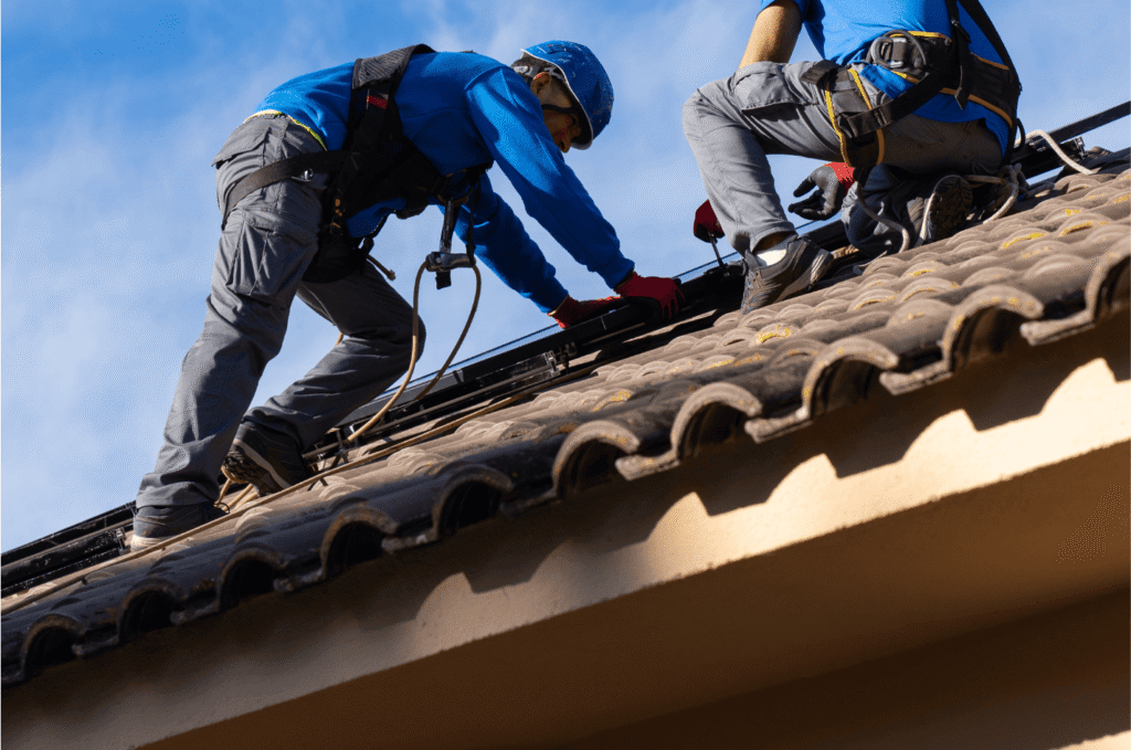 Roofing companies technician installing tiled roofs while workers safely secure equipment during a residential project
