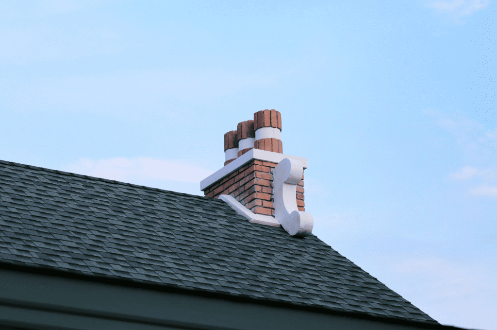 House roof with brick chimney under a clear sky, an area where roof repair is often needed to prevent leaks.