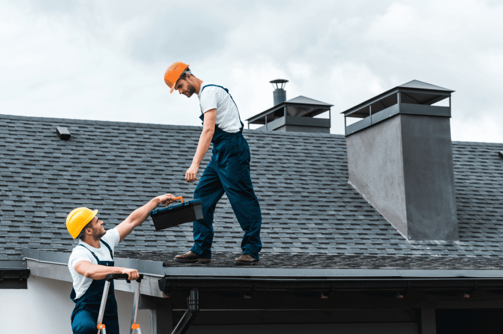 Roofers working on shingles and tools on roof, showing clear roof replacement signs and active repair work.