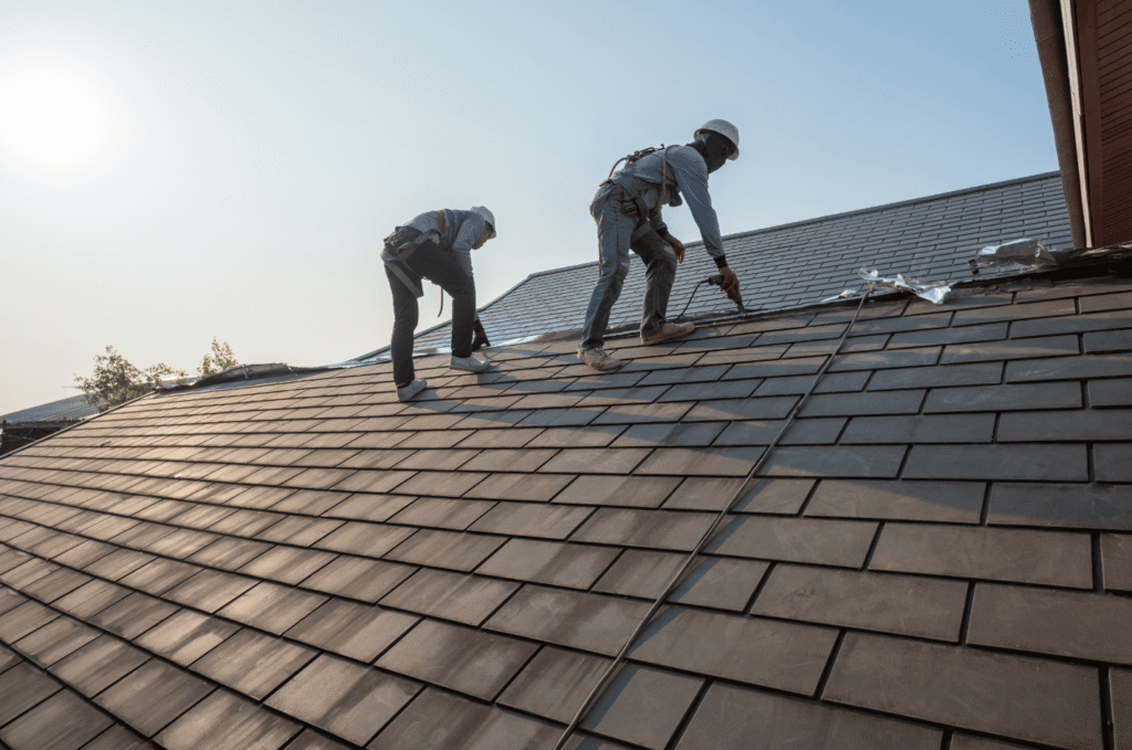 Two workers perform roof repair by securing shingles and sealing joints to protect the roof from leaks and damage.
