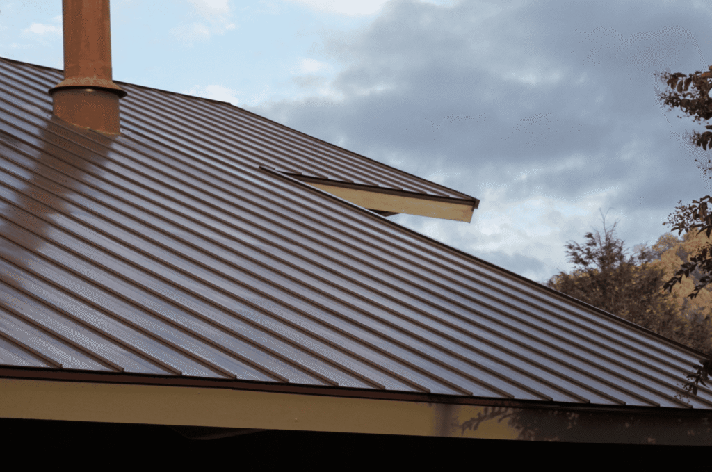 Metal roof with chimney and skylight area shown during a roof inspection to check flashing, seams, and overall roof condition.