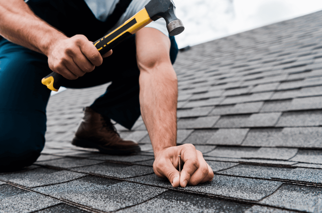 Worker installing nails into an asphalt shingle roof using a hammer to secure shingles and ensure a strong, weatherproof surface