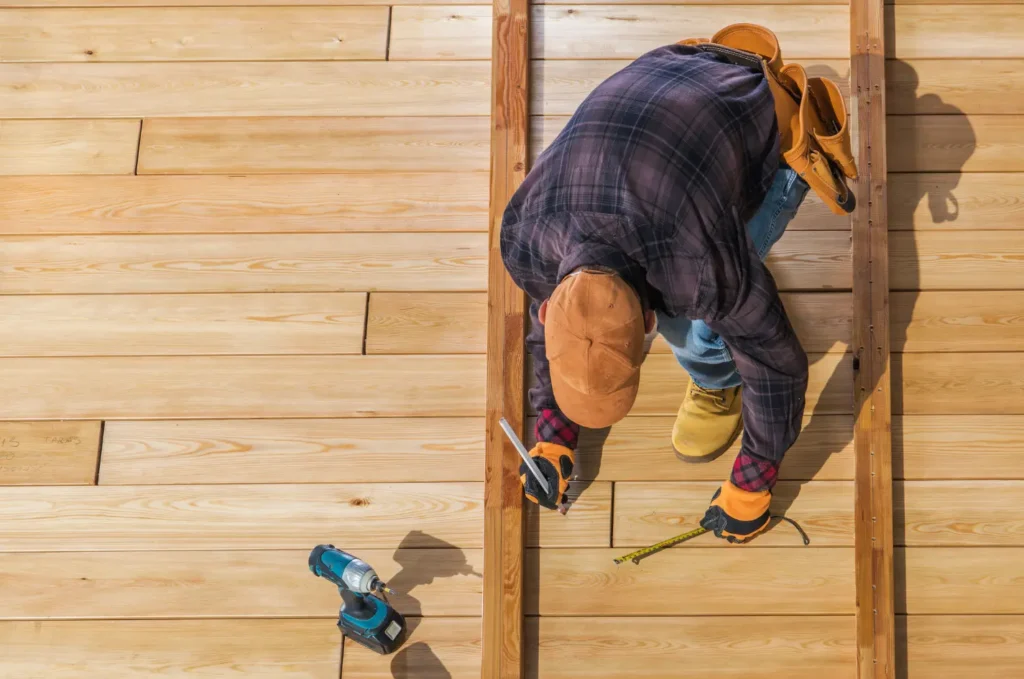 Worker measuring and installing deck boards during deck building, showing precise steps used in deck repair projects