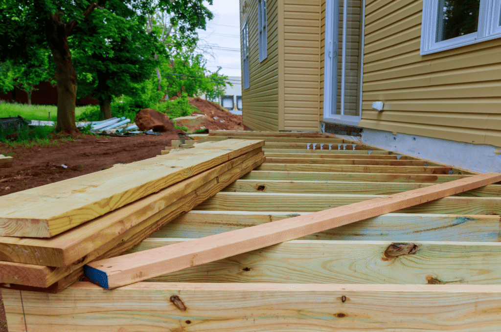 Wood framing in progress during deck building beside a house, showing strong support beams ready for deck boards