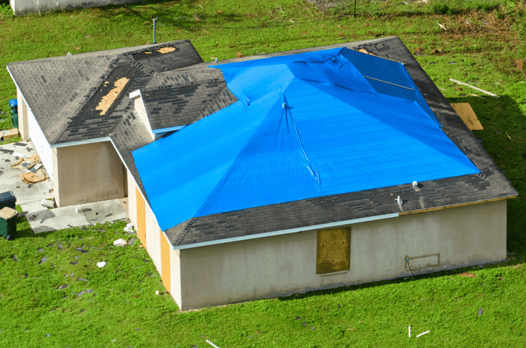 Aerial view of a storm-damaged home with a blue tarp installed over the roof as a temporary roof leak fix