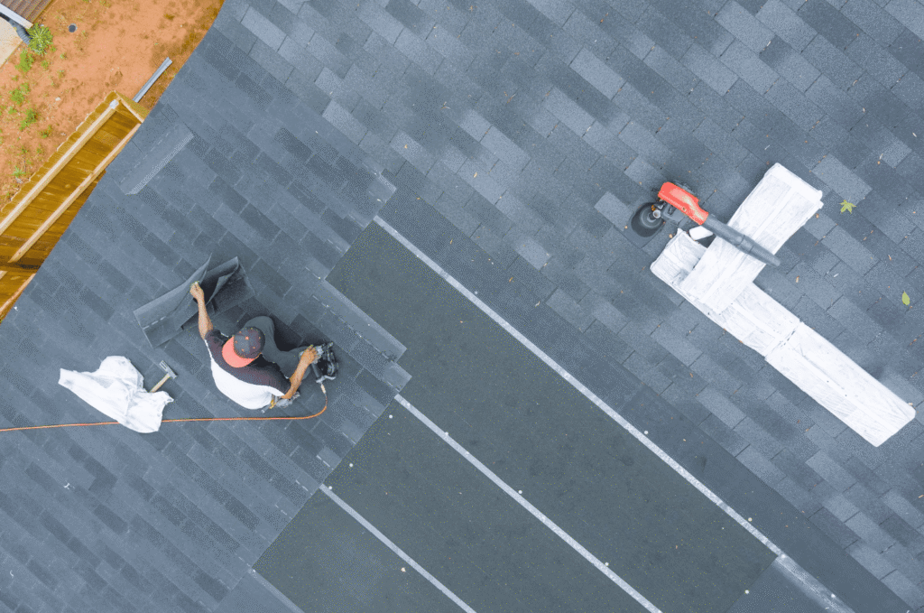 Aerial view of asphalt shingle roof installation with a worker nailing new shingles on a residential property
