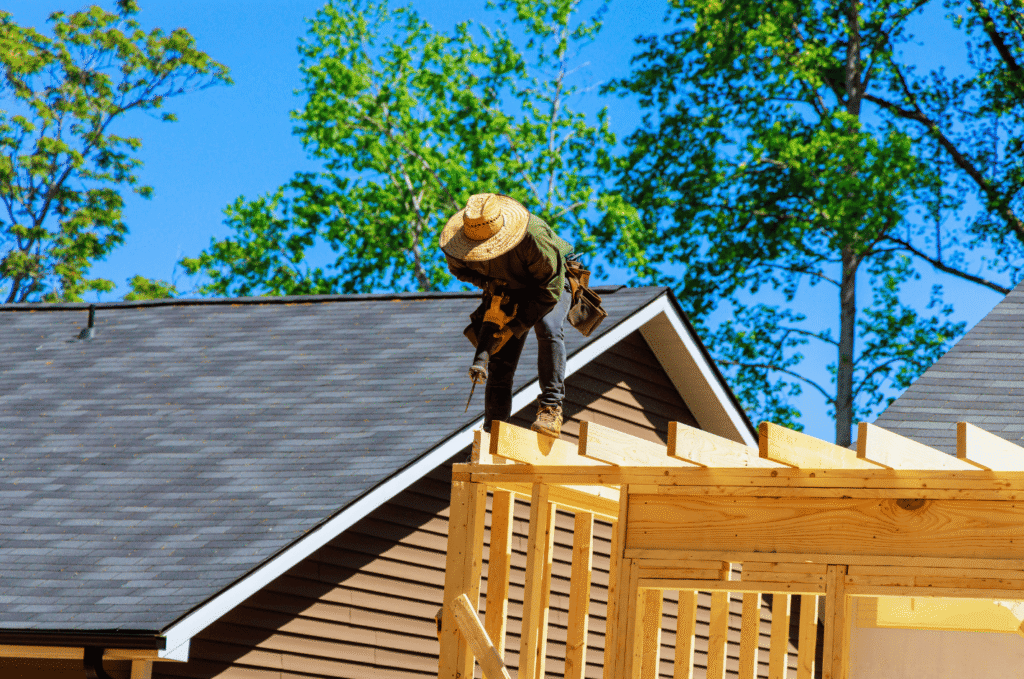 Residential roof installation contractor working on a home with completed asphalt shingles on a sunny day