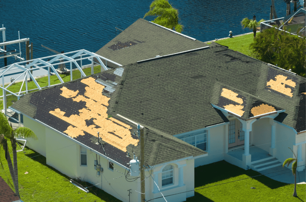 Aerial view of a residential home with severe storm roof damage showing large areas of missing shingles and exposed deck