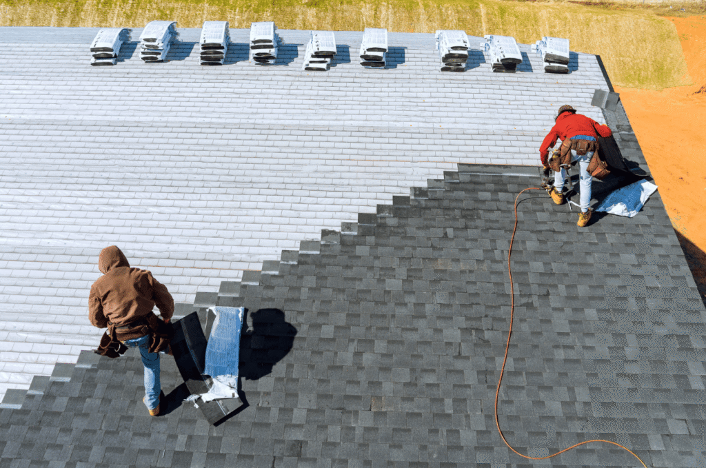 Aerial view of two roofers installing new asphalt shingles with a nail gun during roof repair.