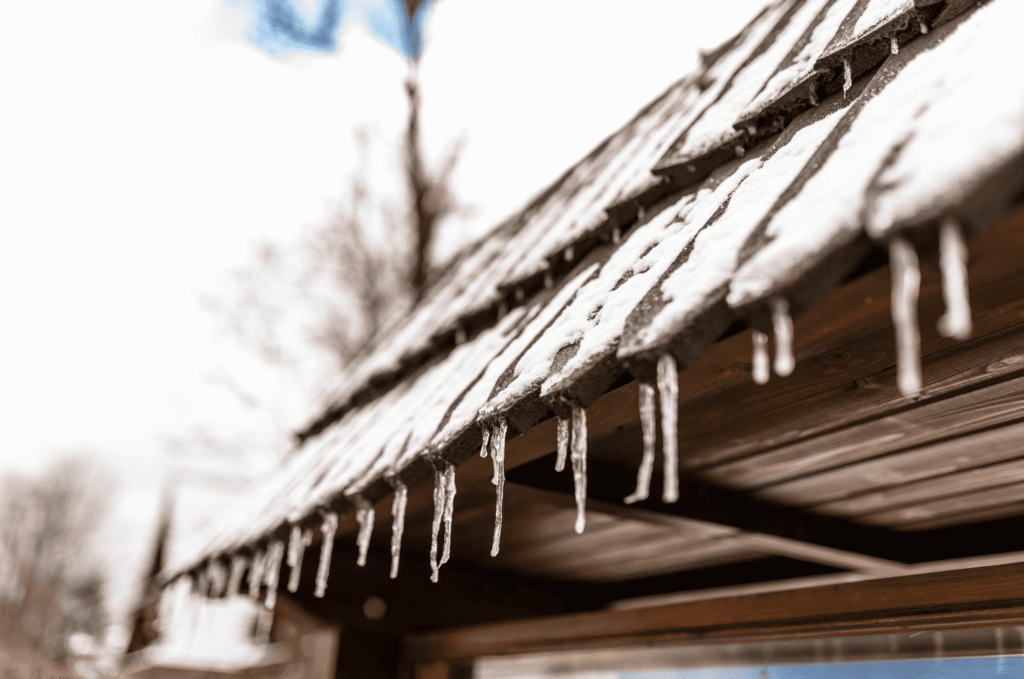 Icicles forming along a snow-covered roof edge showing early signs of ice dam buildup from poor attic ventilation