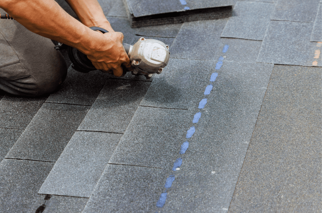 Roofer installing asphalt shingles with nail gun during new roof installation after repeated roof leak repair problems