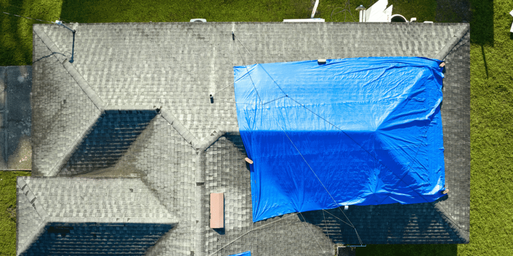Aerial view of a residential roof with a blue emergency tarp covering storm-damaged section secured with ropes and ties