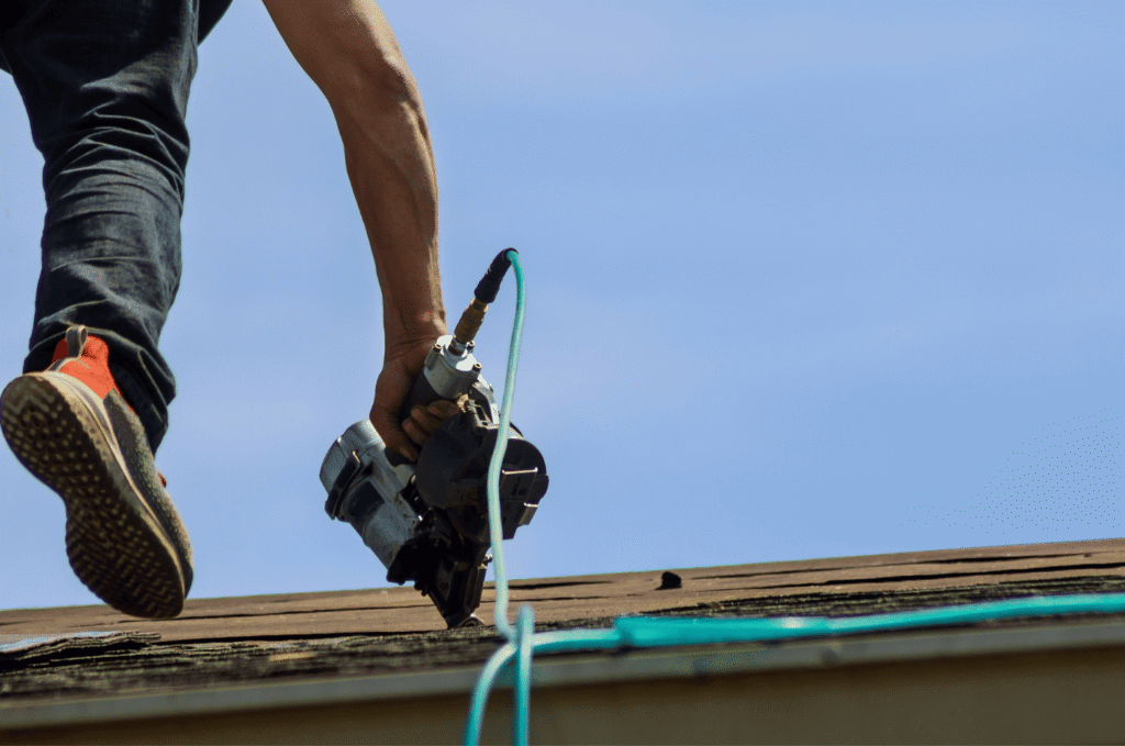 Roofer standing on a roof using a pneumatic nail gun to fix damaged shingles for a temporary roof leak repair