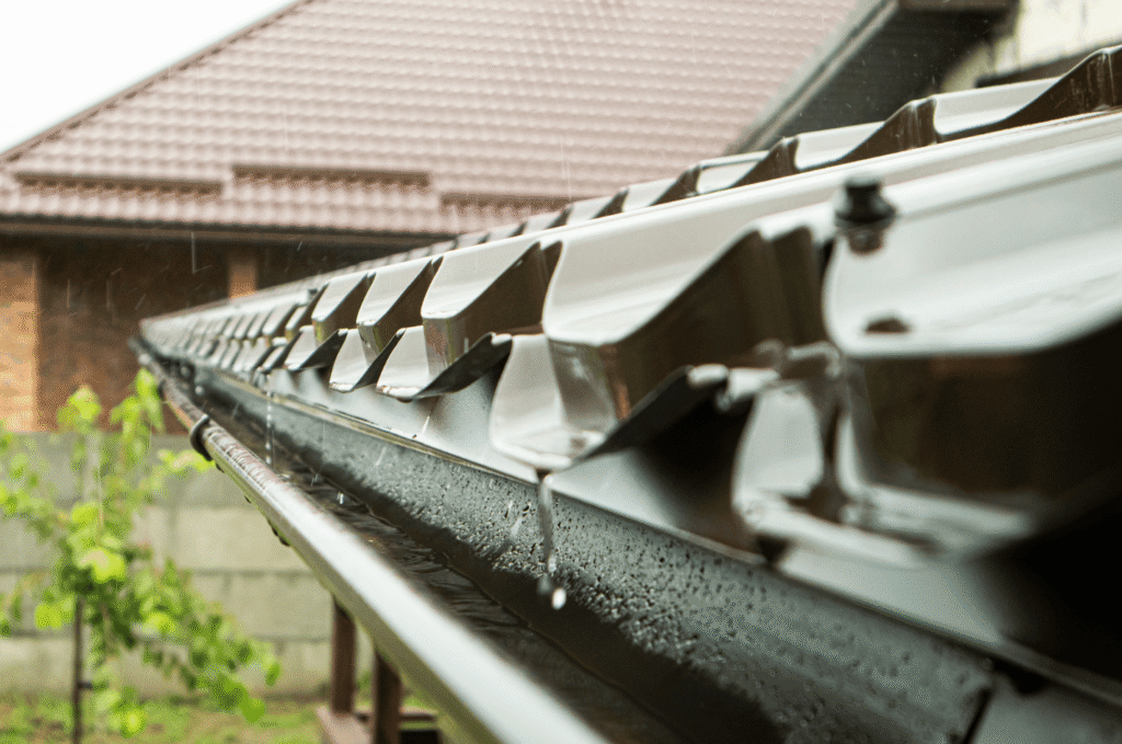 Rain falling on a sloped roof and gutter, showing how roof drainage problems can lead to gutter overflow after Boston storms