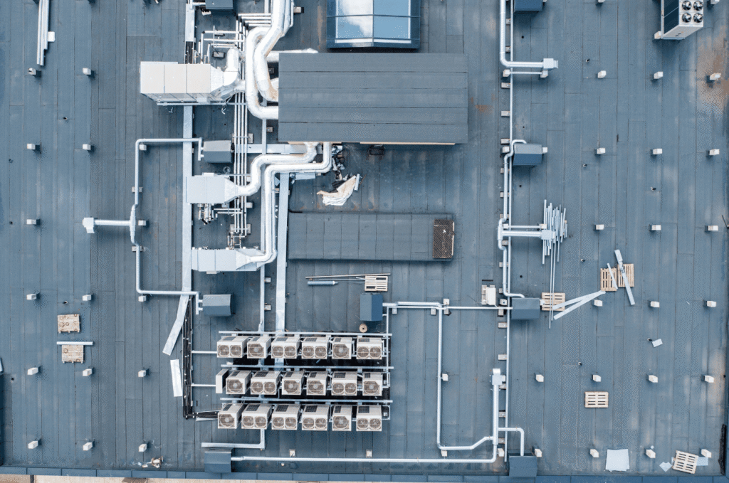 Rooftop HVAC equipment and pipes on a commercial flat roof, showing leak risks, seals, and drainage problems to inspect early 
