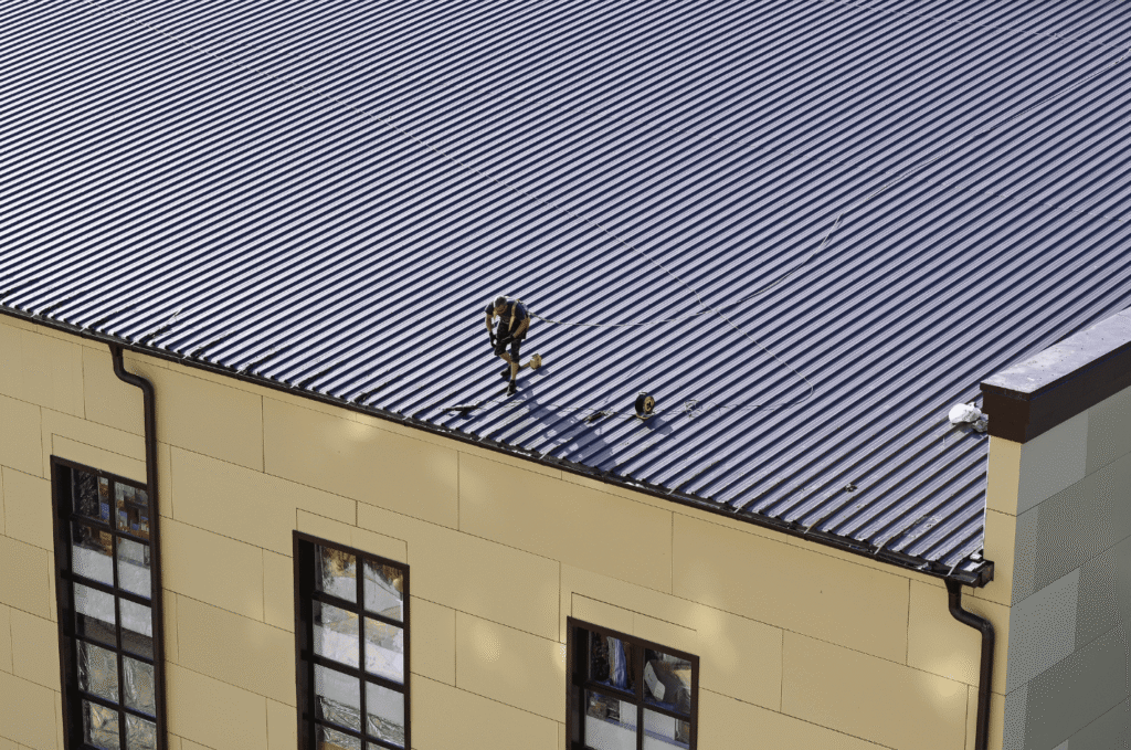 Roofer inspecting a metal commercial roof, showing early signs that need commercial roof inspection before damage spreads