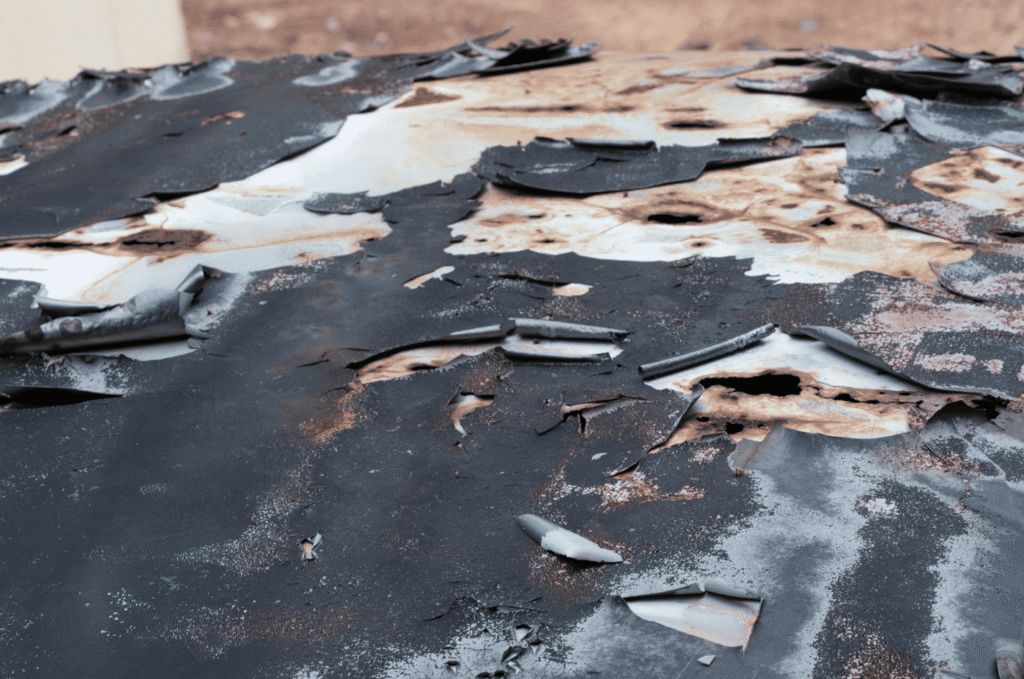 Peeling flat roof membrane with worn surface patches showing blistering risk, trapped moisture, and possible leak damage 